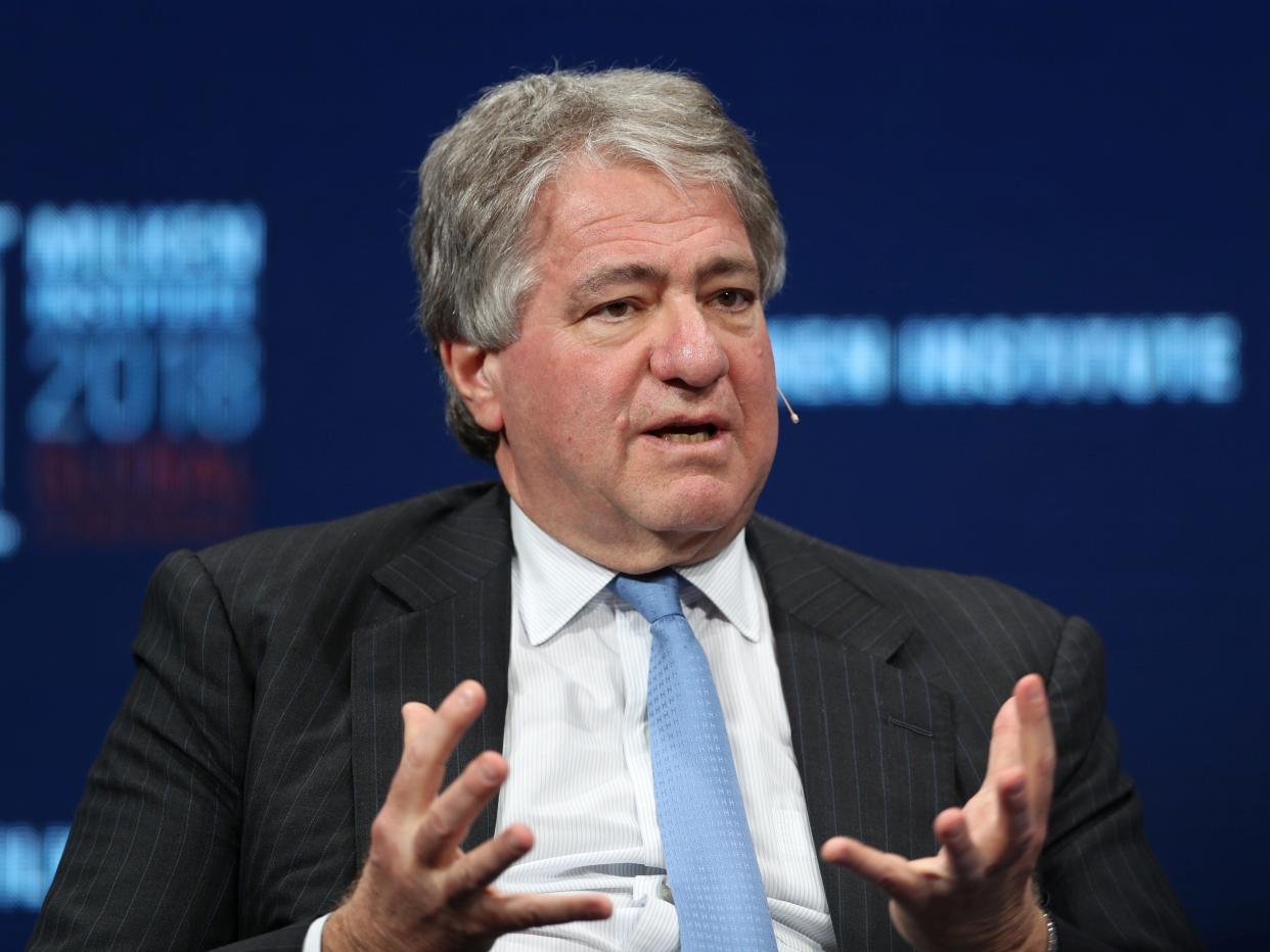 Leon Black wears a dark grey suit, white shirt, and blue tie while speaking on stage.