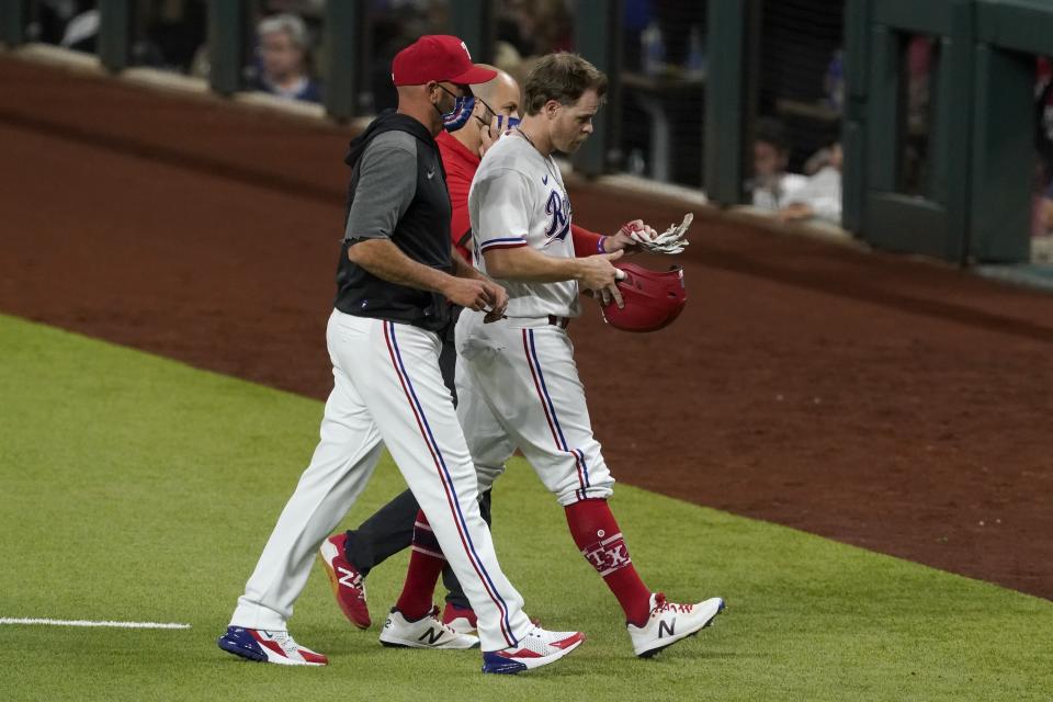 Texas Rangers manager Chris Woodward, left, and a member of the team's staff, rear, escort Brock Holt, right, off the field after Holt hit a single that scored Nick Solak during the eighth inning of the team's baseball game against the Toronto Blue Jays in Arlington, Texas, Tuesday, April 6, 2021. Holt left the game with an unknown injury. (AP Photo/Tony Gutierrez)
