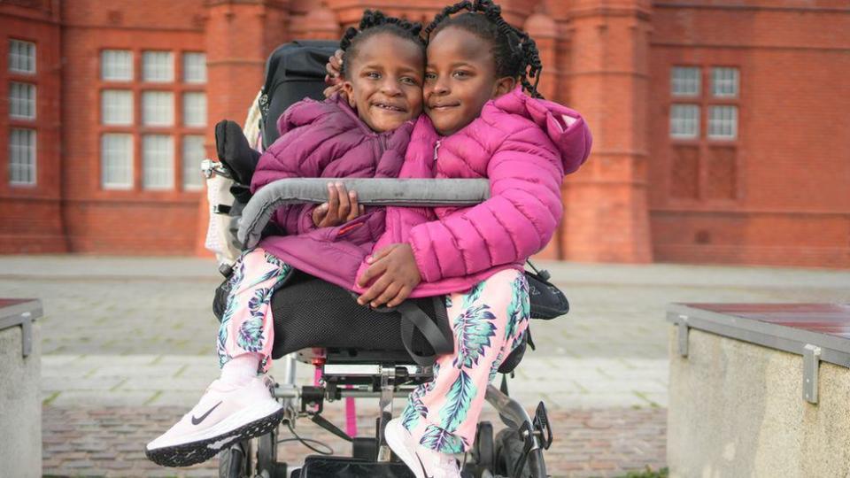 Marieme y Ndeye con chaquetas rosadas sentadas en una silla movible