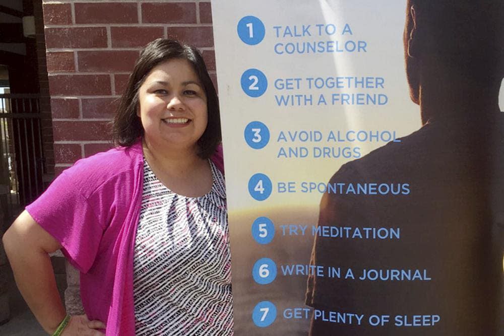In this undated photo provided by Wendy Gonzalez, Alma Lopez, the district’s school counselor coordinator and one of two counselors at Livingston Middle School, poses for a photo beside a mental health banner, in Livingston, Calif. (Wendy Gonzalez via AP)