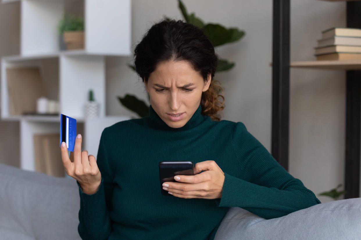 Concerned young hispanic lady looking on smartphone screen having finance savings stolen from bank card as money fraud result. Upset nervous latin woman become online scammers victim