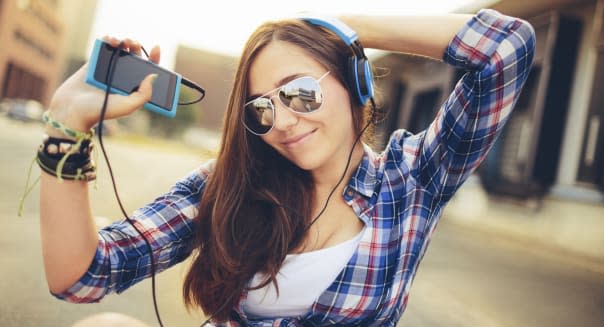 Cheerful teen dancing and moving along with music on her smart phone and headphones