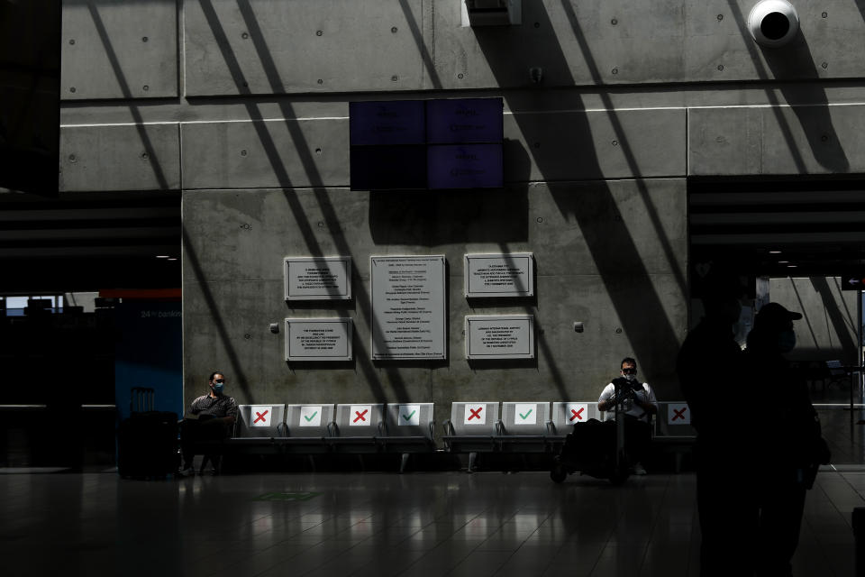 Two men wearing face masks are seated on an airport bench a seat apart in line with social distancing rules at Cyprus' main airport in Larnaca, on Tuesday, June 9, 2020. Cyprus re-opened its airports on Tuesday to a limited number of countries after nearly three months of commercial air traffic as a result of a strict lockdown aimed at staving off the spread of COVID-19. (AP Photo/Petros Karadjias)