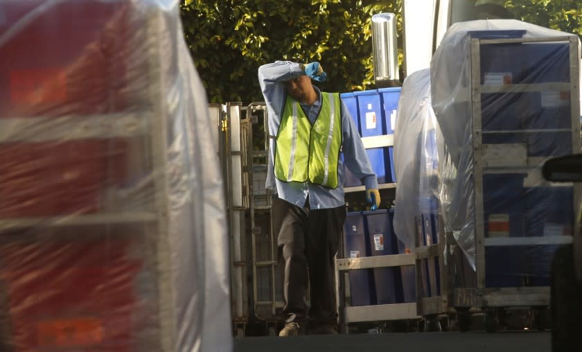 LOS ANGELES, CA - MARCH 25, 2020 - A worker wipes his brow while being surrounded by containers filled with biohazardous waste at Stericycle w in Vernon on March 25, 2020. The company may be dealing with logistical challenges facing medical waste treatment companies during the pandemic. Stericycle, in Vernon, is one of the largest medical waste treatment centers in Southern California. (Genaro Molina / Los Angeles Times)