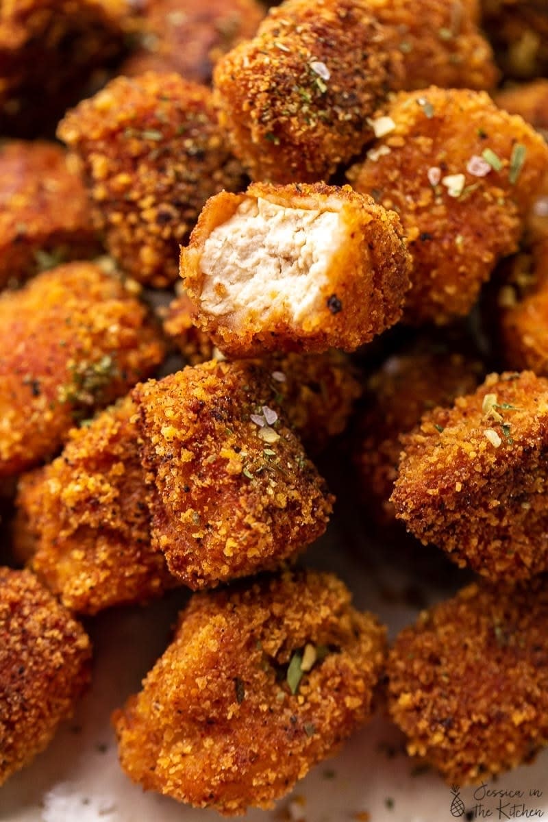 A plate of crispy tofu nuggets with one sliced to reveal a white, moist center