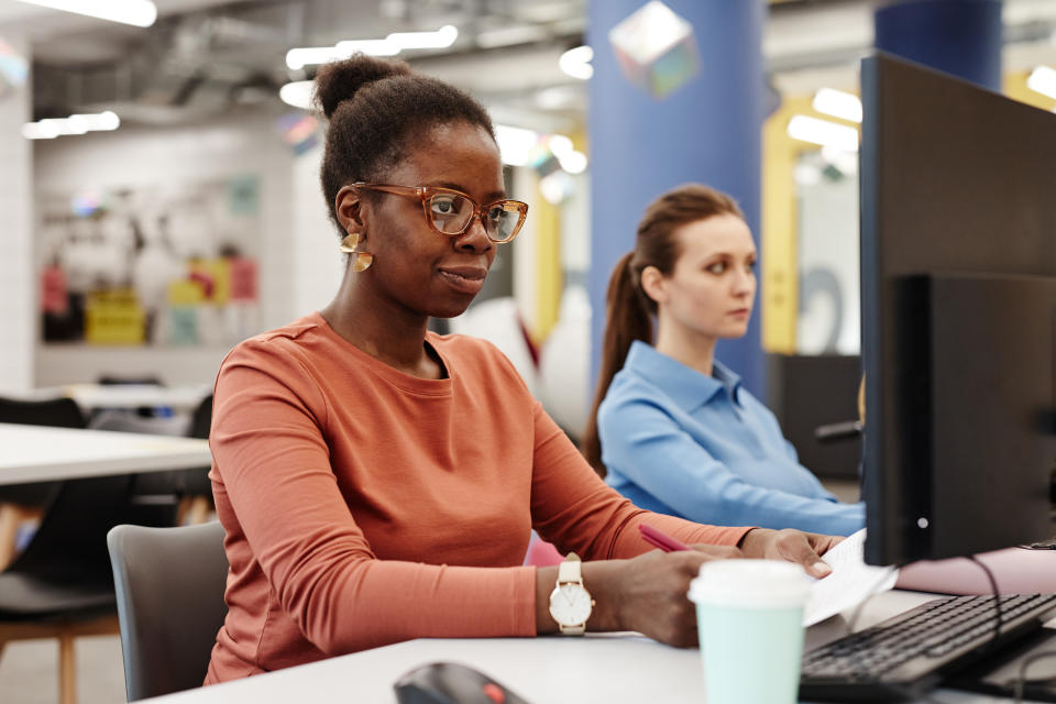 Vibrant portrait of young black woman using computer in college while doing research in library