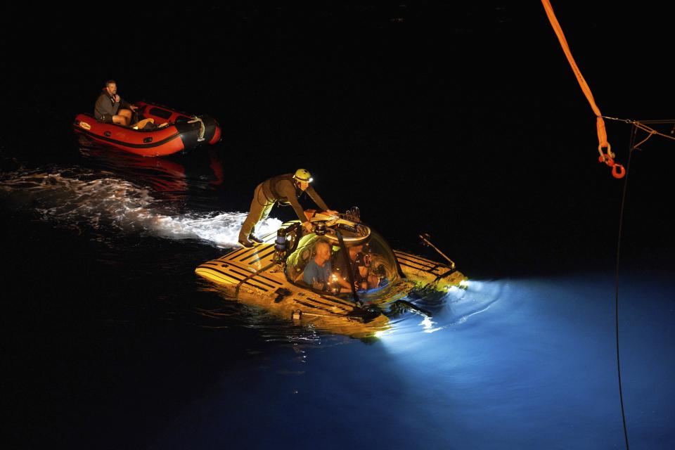 The manned submersible surfaces after dark after a failed mission to recover a stranded ROV (Remotely Operated Vehicle), Wednesday March 13, 2019. The previous day, an accident severed the cable connecting the drone to the mother-ship of the British-based Nekton mission. The camera-carrying ROV is a vital image-gathering tool that can go deeper than the submersibles. (AP Photo/David Keyton)