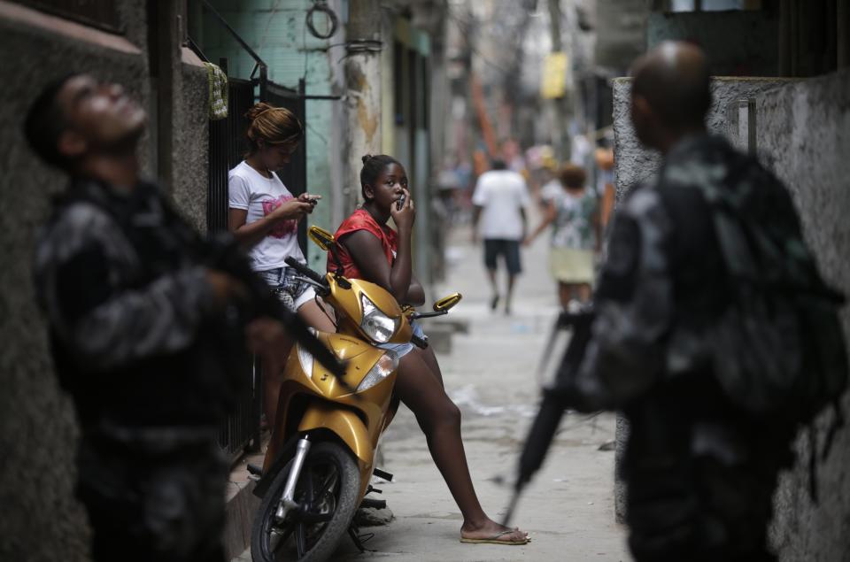 Girls rest along an alley as police officers patrol during an operation at the Mare slums complex in Rio de Janeiro