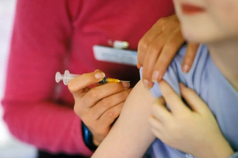 A child about to be given the MMR (mumps, measles, rubella) vaccination into their arm by a surgery nurse with a hypodermic syringe, England, UK.