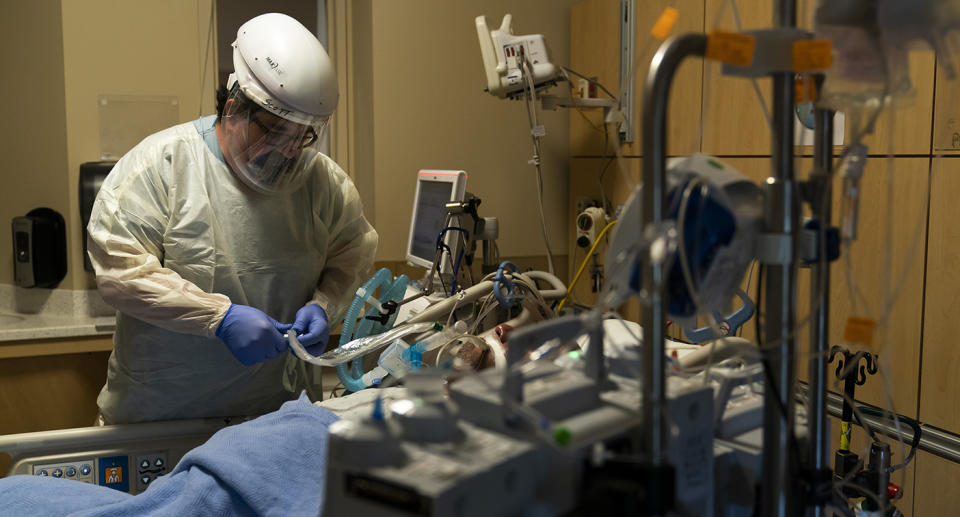 Doctor wearing PPE shown with patient on ventilator.