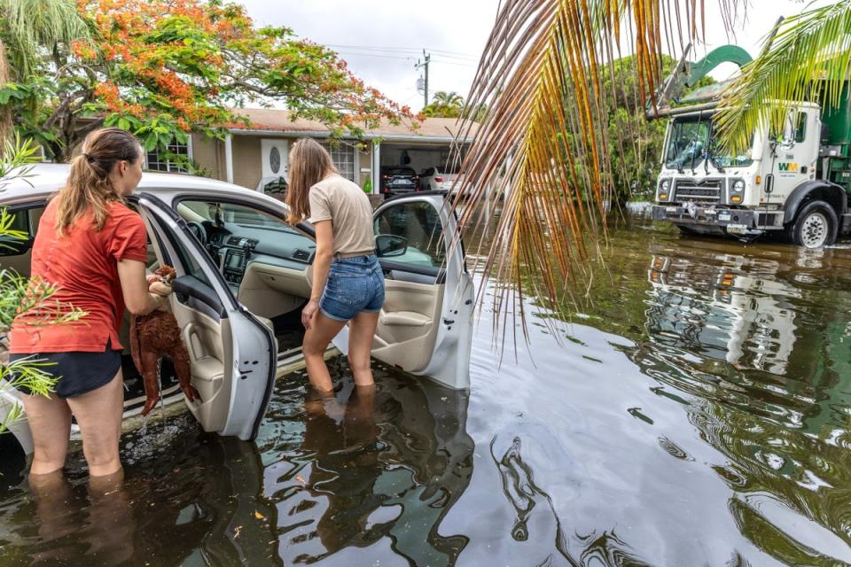 Two people stand next to a car in a flooded neighborhood in Hallandale Beach, Florida (EPA)