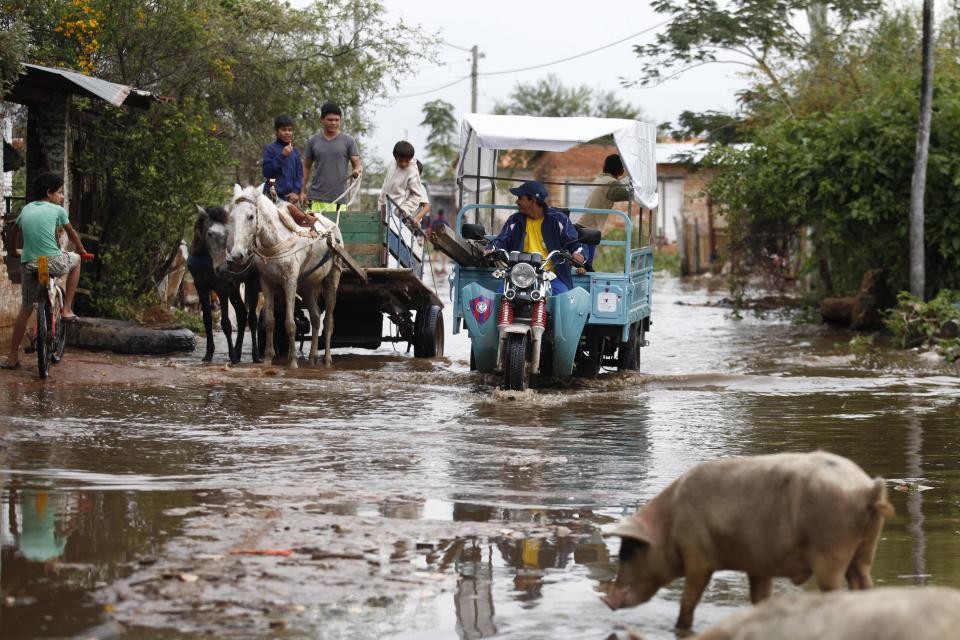 In this July 9, 2013 photo, people cross a flooded road in a horse-drawn cart and a motorcycle in the Santa Ana neighborhood of Asuncion, Paraguay. The city is phasing out the horse-drawn carts that are used by people who collect recyclable material and is sending the horses to an equine sanctuary. The initiative by Asuncion’s municipal government is being hailed by animal rights activists. (AP Photo/Jorge Saenz)