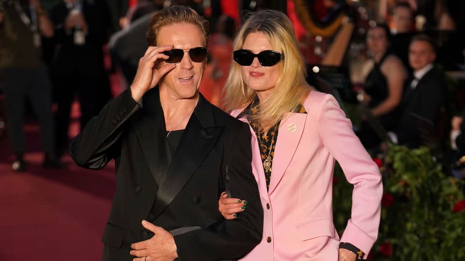 Actor Damian Lewis (left) wears a black Lanvin suit jacket and yellow trousers while walking down the red carpet with singer-songwriter Alison Mosshart (right), who rocked a pink suit and orange and black star-spangled shirt. - Yui Mok/AP