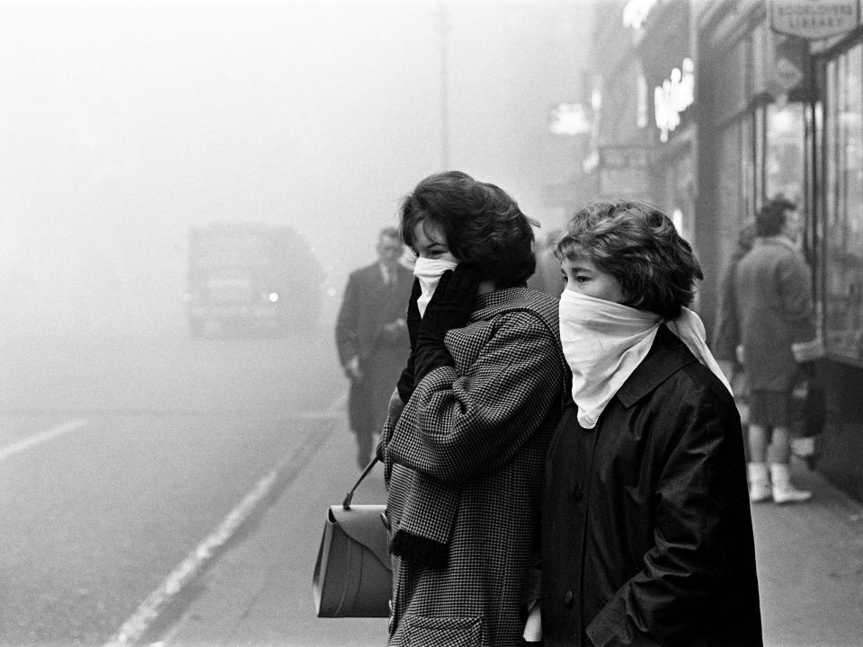 Two women wear masks as a haze obscures cars behind them in London in 1962.