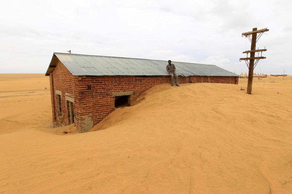 A worker rests on the roof of a building surrounded by sand at Ogrein Railway Station in Sudan