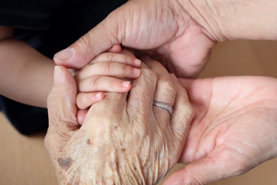 Four hands from different age groups are gently holding each other, symbolizing unity and connection across generations