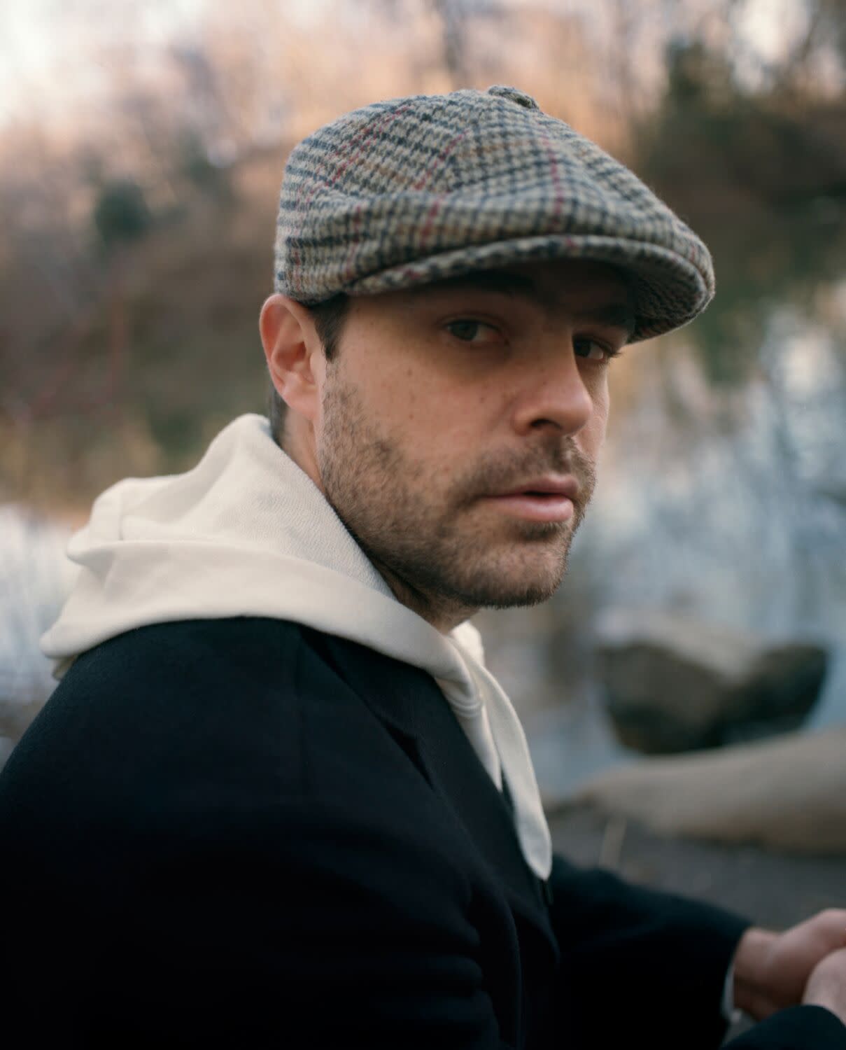 A man in a cap and scarf poses outside for a portrait.