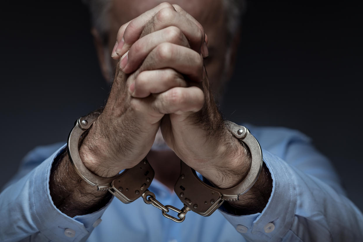 An elderly man in handcuffs.