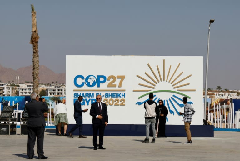 Homens e mulheres em frente à painel da COP27 (Foto: AFP/Ludovic MARIN)