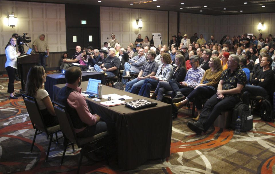 In this Monday, April 8, 2019, photoHolly Prohaska, at podium left, a project manager for a Bureau of Land Management contractor that helped prepare a draft environmental impact statement for the Burning Man festival, describes the document during a public hearing in Sparks, Nev. Nearly 200 Burning Man backers packed a casino meeting room to mostly complain about new conditions and restrictions the government wants to place on the counter-culture festival in the northern Nevada desert. (AP Photo/Scott Sonner)