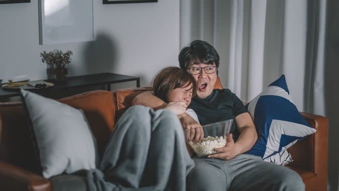 couple watching scary horror tv show at night during weekend in living room sitting on sofa