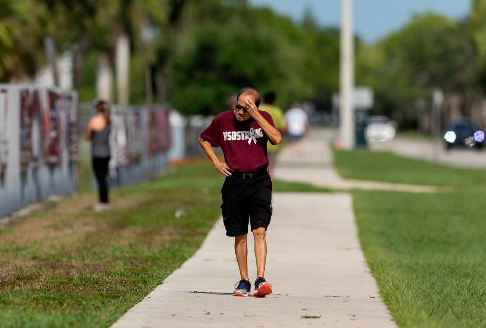 A pedestrian walks down Holmberg Road as crews use heavy equipment to tear down the 1200 building of Marjory Stoneman Douglas High School on Friday, June 14, 2024, in Parkland, Fla. On February 14, 2018, a gunmen entered the school and killed 17 people.