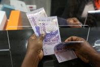 A woman holds money as she performs a financial transaction at a bank of the French mobile operator Orange in Abidjan, Ivory Coast