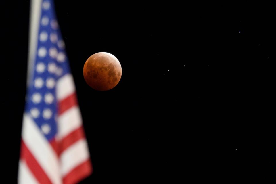 A full moon is seen approaching totality framed with a US flag during a total lunar eclipse as the moon enters Earth's shadow for a super blood moon on May 26, 2021, in Chico, California.