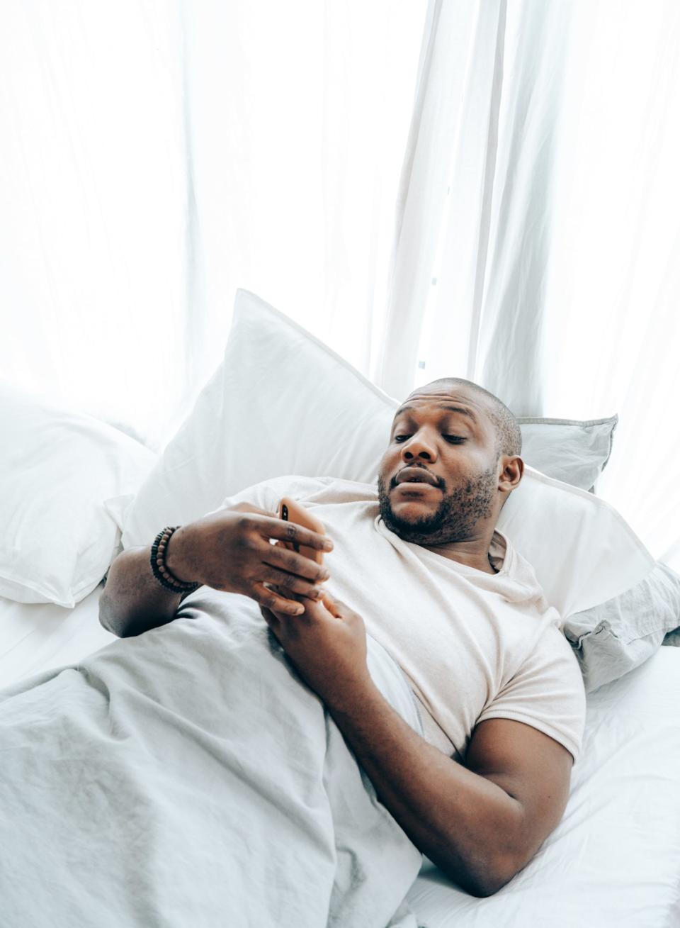 Black man staring at his phone while laying in the bed