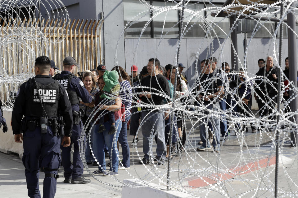 FILE - In this Nov. 19, 2018, file photo, people line up to cross into the United States from Tijuana, Mexico, seen through barriers topped with concertina wire at the San Ysidro port of entry in San Diego. U.S. immigration authorities say the number of people expressing fear of returning home when they are stopped at the Mexican border spiked in the last year. (AP Photo/Gregory Bull, file)