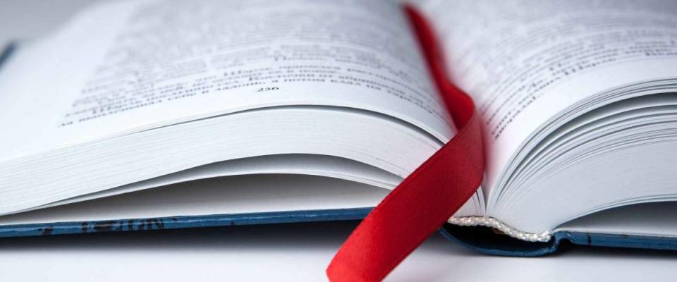 new open book on a gray table with a red ribbon bookmark close up