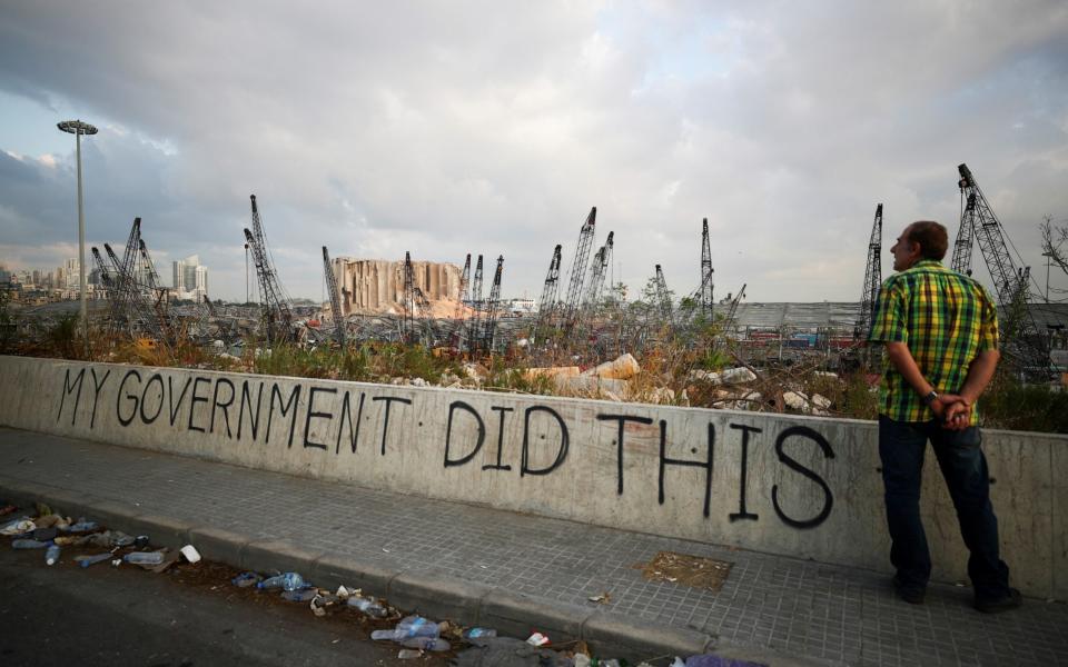 A man stands next to graffiti at the damaged port area in the aftermath of a massive explosion in Beirut
