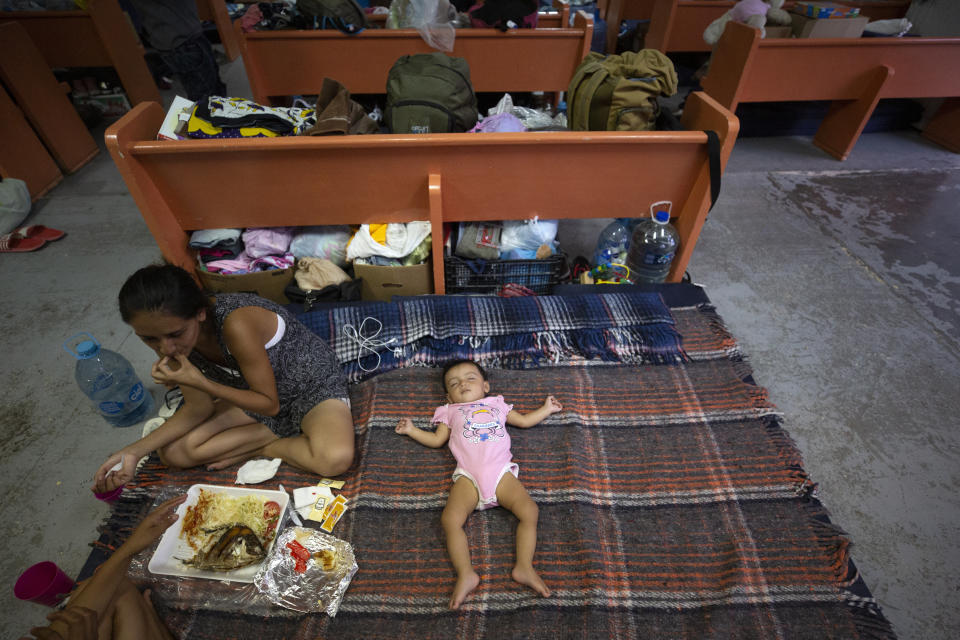 In this July 28, 2019, photo, Evelyn, of El Salvador, eats a shared lunch as her daughter sleeps an area set up for families among the pews at El Buen Pastor shelter for migrants in Cuidad Juarez, Mexico. (AP Photo/Gregory Bull)