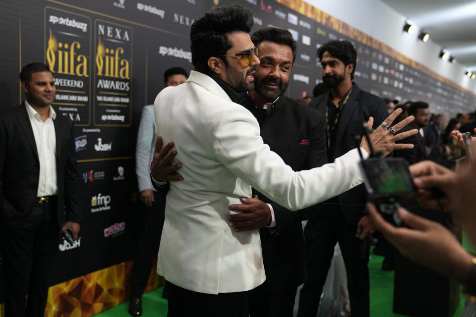 Indian actor and presenter Manish Paul, in white jacket, hugs actor Bobby Deol as they arrive on the green carpet ahead of the 22nd International Indian Film Academy (IIFA) awards in Abu Dhabi, United Arab Emirates, Friday, June 3, 2021. (AP Photo/Kamran Jebreili)