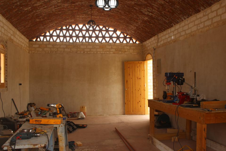 A Hand Over–built farmhouse in Giza, Egypt. The client, Kiwa, is an agricultural organization aimed at introducing new processes to save water and resources in producing organic crops. Most building materials were sourced close to the building site, and the main technique is rammed earth, with the foundation constructed using limestone bricks. Its curved roof and patterned screen are characteristic of passive design, as the feature makes for better ventilation.