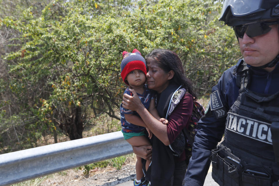 A Central American migrant woman and her son walk with a Mexican Federal Police agent as they are taken into custody on the highway to Pijijiapan, Mexico, Monday, April 22, 2019. Mexican police and immigration agents detained hundreds of Central American migrants Monday in the largest single raid on a migrant caravan since the groups started moving through Mexico last year. (AP Photo/Moises Castillo)