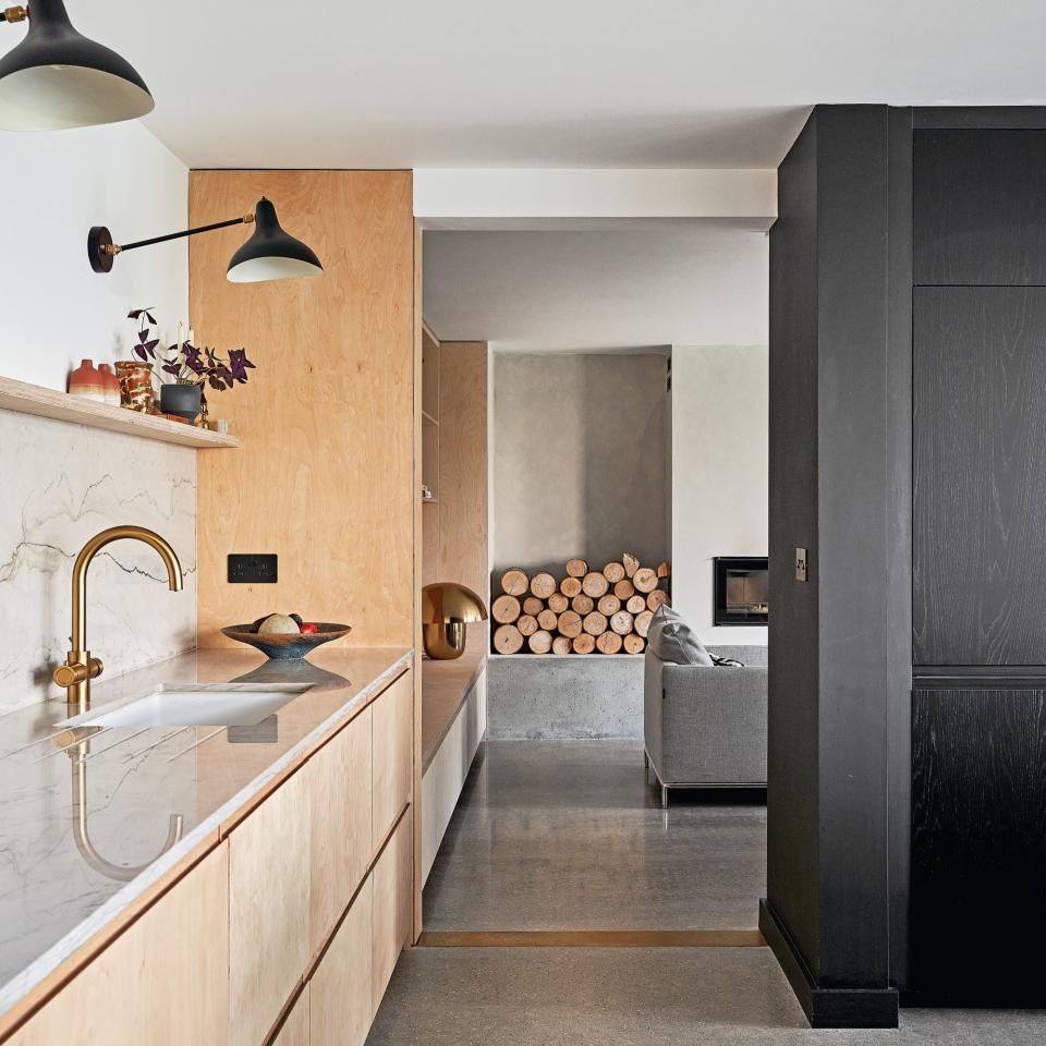 wooden kitchen cabinets with marble worktop leading to snug area with logs