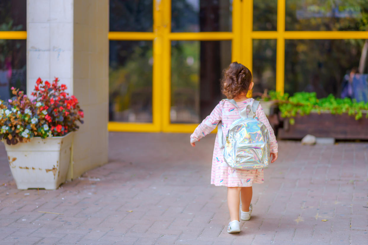 Curly cute little toddler girl back to school with holographic schoolbag or satchel, child going to kindergarten. Toddler kid first day at school or preschool.