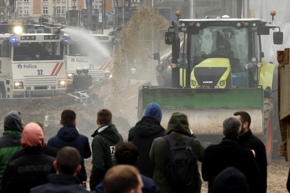 Police use a water canon on a farmer in a tractor spraying hay and manure during a demonstration near the European Council building in Brussels, Tuesday, March 26, 2024. Dozens of tractors sealed off streets close to European Union headquarters where the 27 EU farm ministers are meeting to discuss the crisis in the sector which has led to months of demonstrations across the bloc. (AP Photo/Geert Vanden Wijngaert)