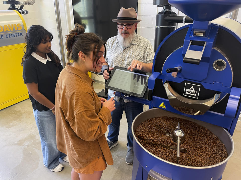 Timothy Styczynski, Head Roaster, UC Davis Coffee Center displays a coffee bean roasting machine to Shrishti Chezhian, UC Davis Senior, left and graduating student Kiara DeGroen, at the Coffee Center at UC Davis in Davis, Calif. on Monday, June 17, 2024. The center which opened last month, is believed to be the first coffee-only research facility opened on any college campus in the U.S. (AP Photo/Haven Daley)