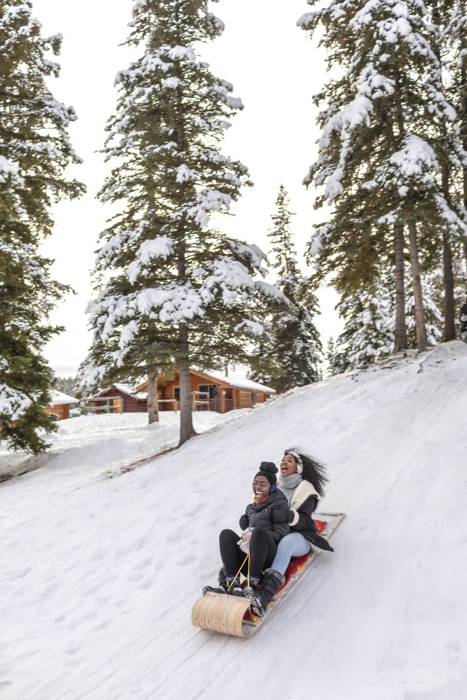 two excited woman ride wooden sled down snowy hill