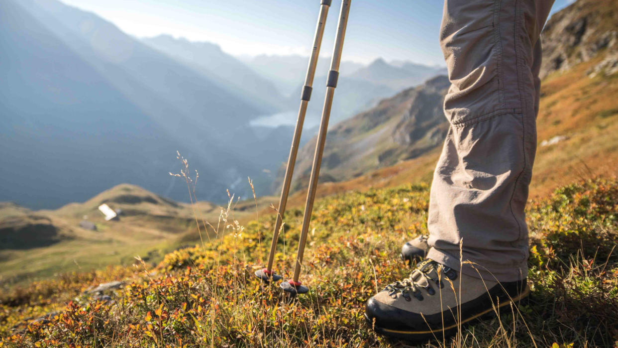  Hiking shoes and walking poles, with view over the dam of Tignes. 