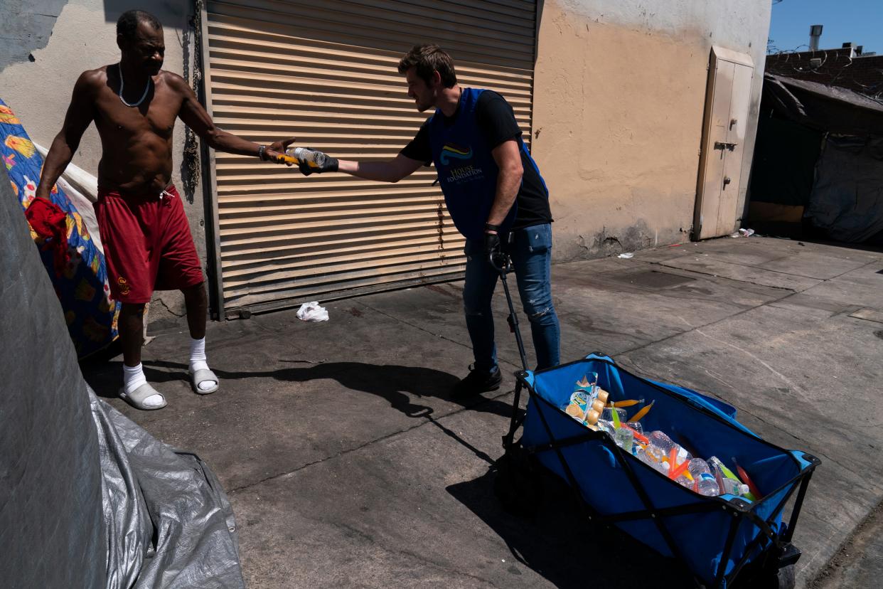 Paskal Pawlicki from My Friends House Foundation, hands a bottle of water to a homeless man in the Skid Row area of Los Angeles, Wednesday, Aug. 31, 2022.