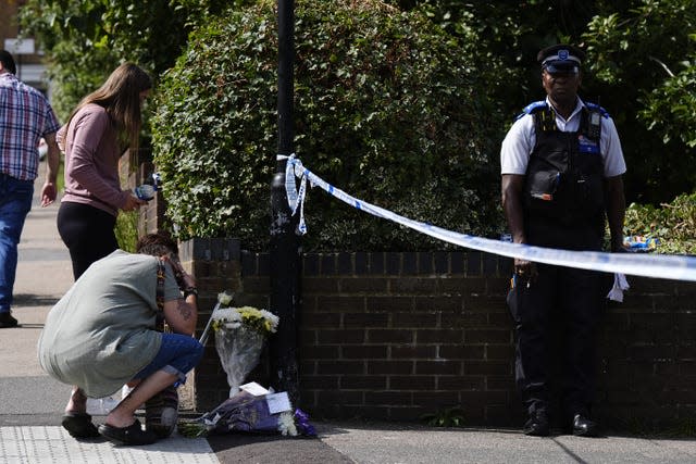 Police officer stands by a cordon as a member of the public lays flowers