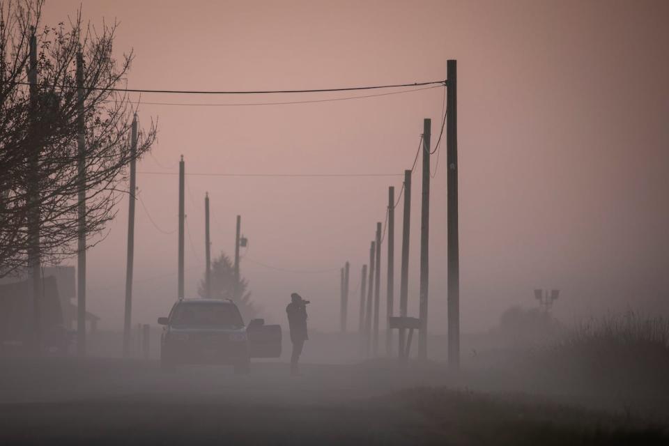 A woman takes a pictured on the side of a road during a period of dense fog in Surrey, British Columbia on Monday, November 27, 2023. 