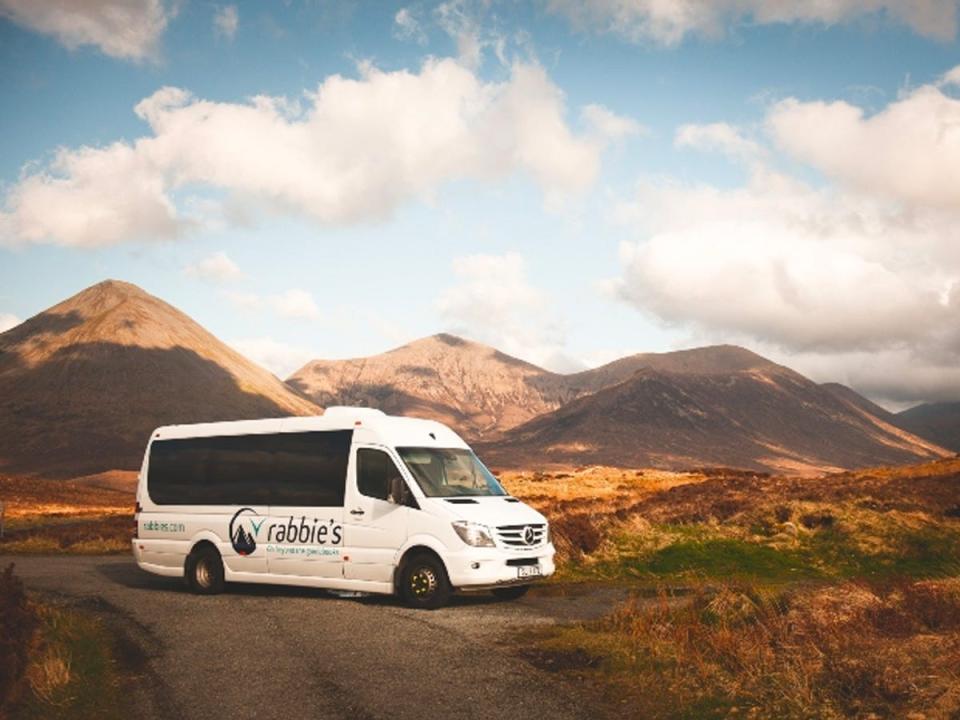 A Rabbie's tour van parked along the side of a road overlooking mountains of the Scottish Highlands.