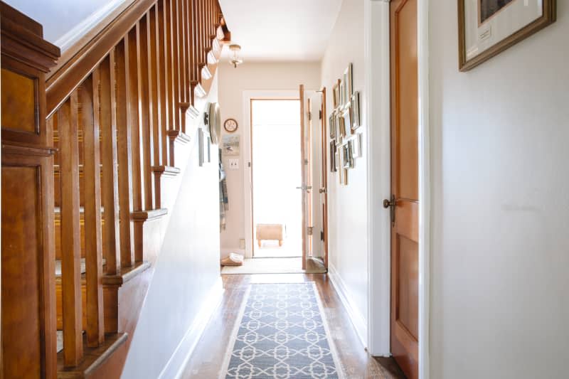 A door opens and leads to an elongated hallway where a runner or area rug can be seen