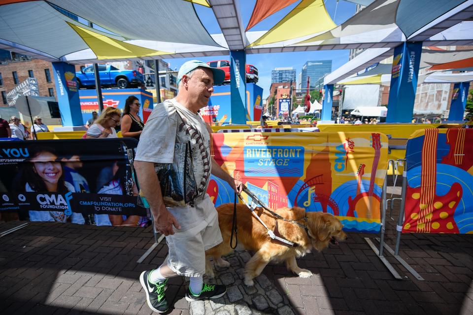 Scott Hegle and his guide dog, Lumiere, navigate through the entrance of Riverfront Park at the CMA Fest in Nashville, Tenn., Saturday, June 11, 2022.