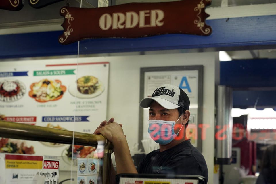 A worker wears a mask while while waiting to taker orders in a deli amid the COVID-19 pandemic Thursday, May 20, 2021, at The Farmers' Market in Los Angeles. California regulators will shoot for a mid-June easing of workplace masking and social distancing requirements to conform with a broader state order. They asked to delay a debate Thursday on how quickly they should drop coronavirus safety rules for employees. (AP Photo/Marcio Jose Sanchez)