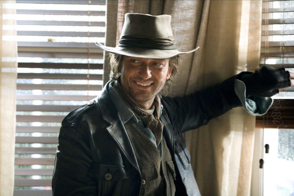 A man in a cowboy hat and traveler's clothes smiles near a window